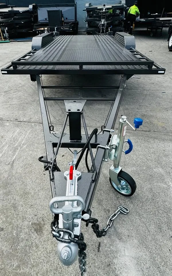 Rear three-quarter view of black 16ft car trailer with perforated checker plate deck in manufacturing yard.