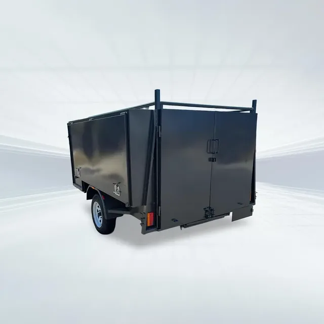 Studio rear angled view of black 7x5 lawn mowing trailer with barn doors and slide-in ramps on white background.